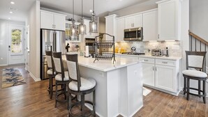 A modern kitchen with white cabinetry, stainless steel appliances, and pendant lighting.