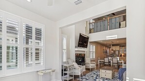A spacious living area with a high ceiling, a dining area, and a kitchen visible through an open door.