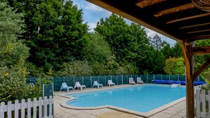 Ein Swimmingpool mit weißem Zaun, umgeben von Grünpflanzen und einem überdachten Bereich mit Stühlen.