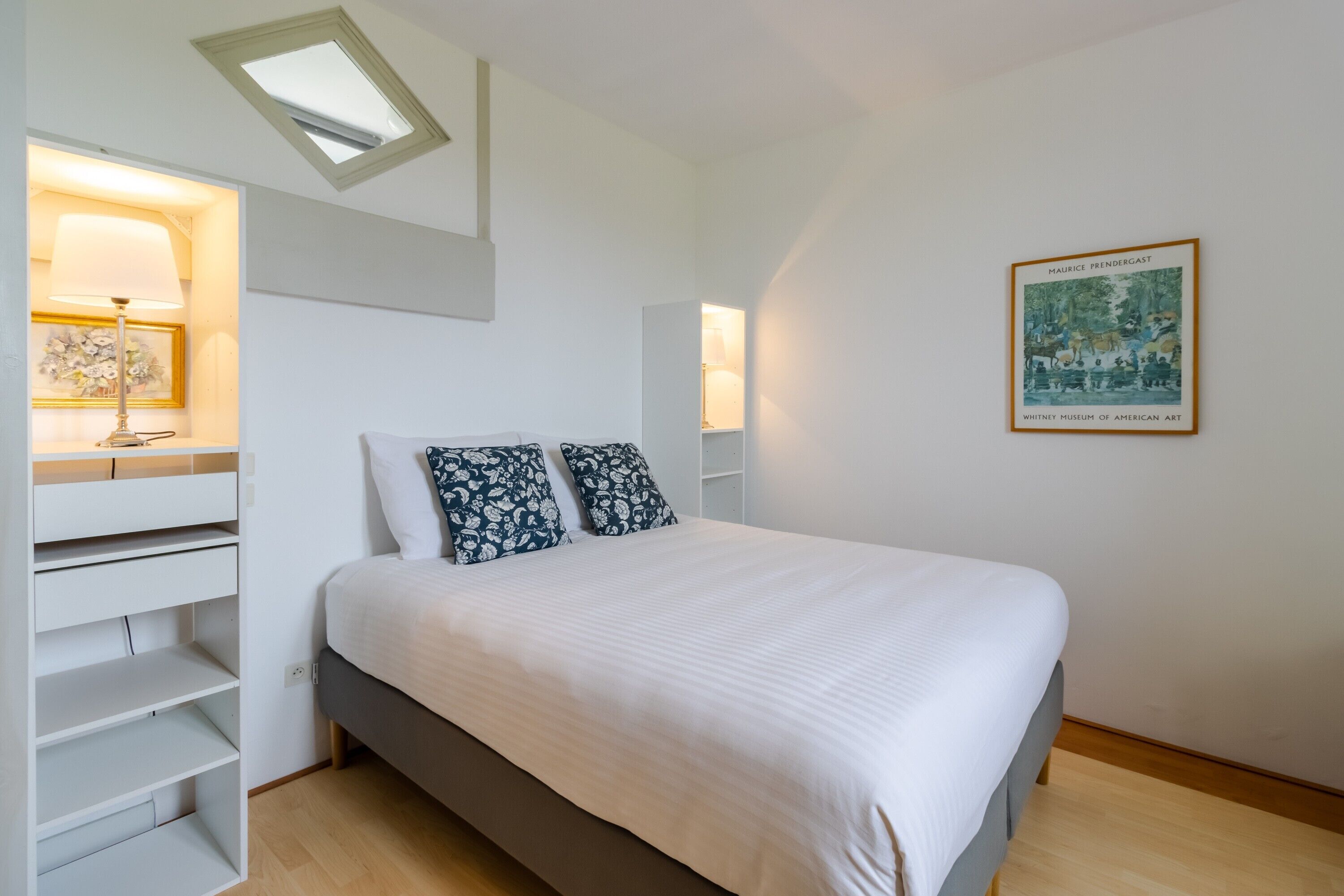 Un dormitorio con cama, estanterías empotradas, tragaluces e imagen enmarcada en la pared.
