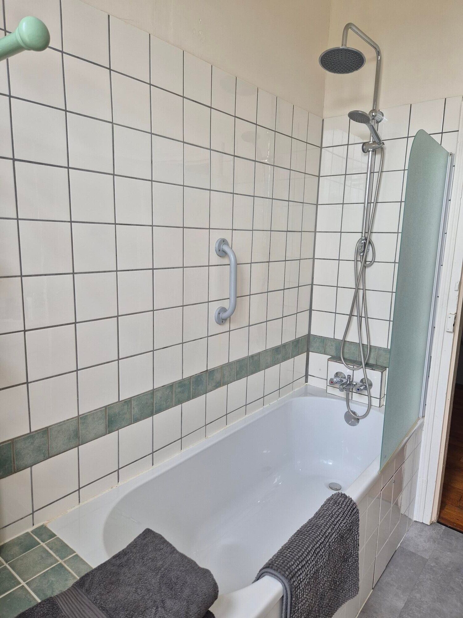 A bathroom with a bathtub, a shower, and a handrail.