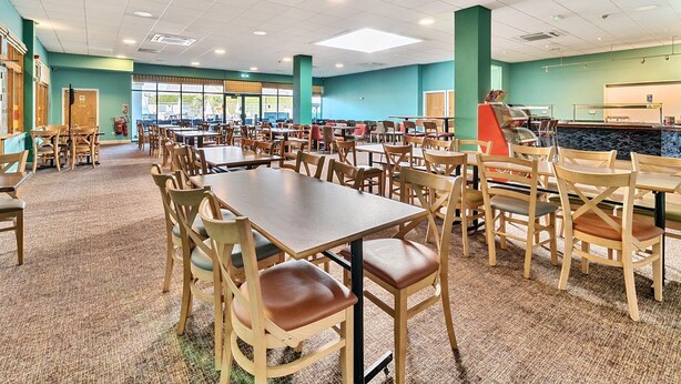 Una cafetería amplia con varias mesas y sillas, una máquina expendedora y una barra con un menú.