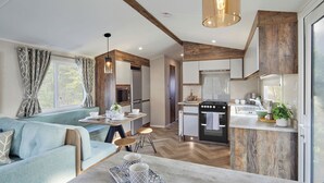 A modern kitchen with wooden accents, a dining area with a blue sofa, and a breakfast bar. - Island Breeze - Hayling Island (Hayling Island)