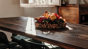 A kitchen with a wooden table, a basket of fruit, and a window with open shutters.