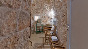 A stone-walled bathroom with a wooden bench, a sink, and a small window.