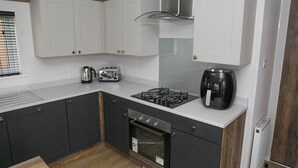 Une cuisine compacte avec des meubles blancs, une cuisinière à gaz, un grille-pain, une bouilloire et une machine à café.