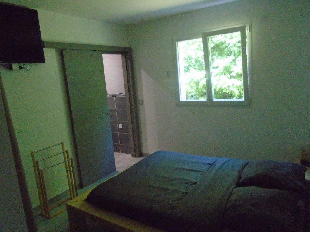 A bedroom with a bed, a window, and a door leading to another room.