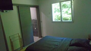 A bedroom with a bed, a window, and a door leading to another room.