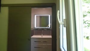 Een badkamer met een spiegel, wastafel en een deur naar een andere kamer.