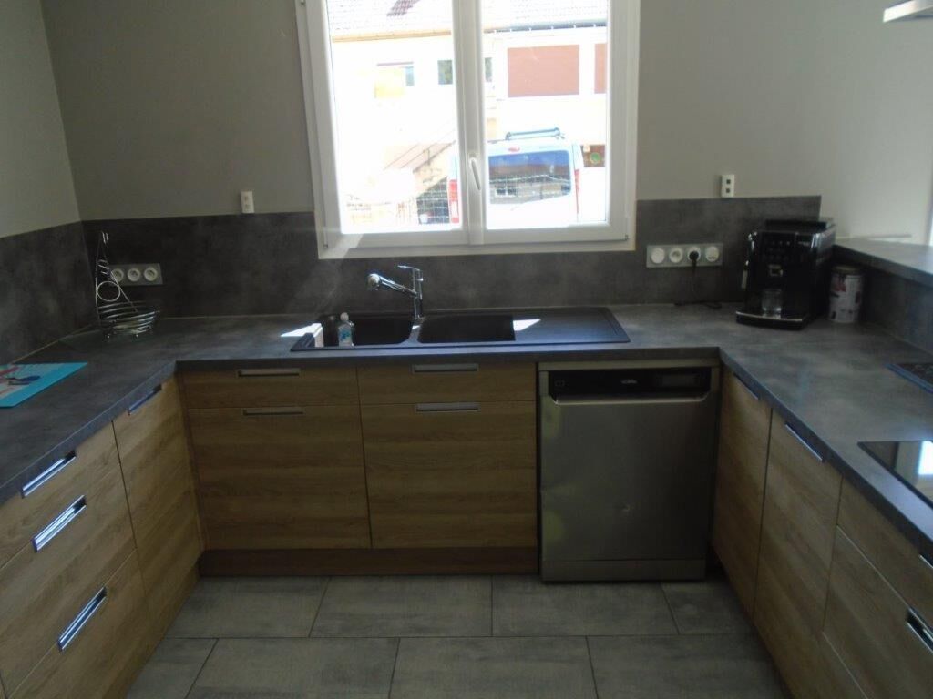 A kitchen with wooden cabinets, a stainless steel dishwasher, and a window with a view of buildings outside.