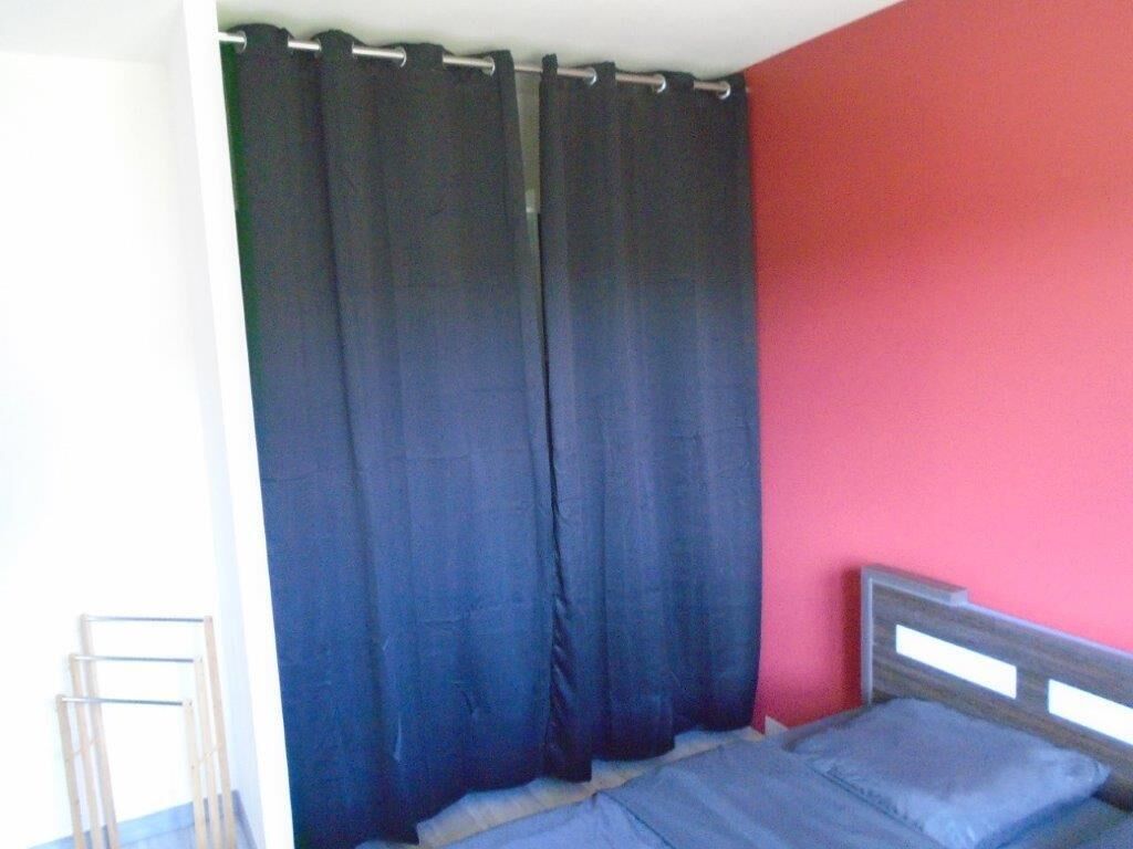 Une pièce avec un lit, un rideau et un mur rouge.