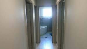 Een smalle gang die uitkomt bij een badkamer met een bad en een toilet.