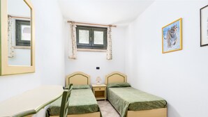 A room with two single beds, a small table, a chair, a window with curtains, and a framed picture on the wall. - Apartment 'Sa Curcurica' (Cala Liberotto)