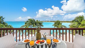 Un balcon offrant une vue sur un paysage tropical, une table dressée pour le petit-déjeuner et une piscine en arrière-plan.