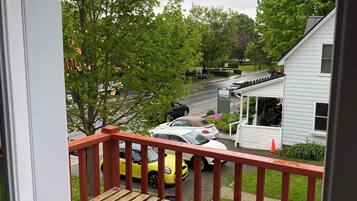 Eine Holzterrasse mit roter Geländer, mit Blick auf eine Straße mit parkenden Autos und Häusern.