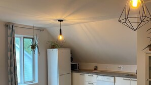 A modern kitchen with a wooden dining table and chairs, a hanging light fixture, and a view of the outdoors through a window. - Apartment for rent in Bromont - 1 bedroom 1 bathroom (Bromont)