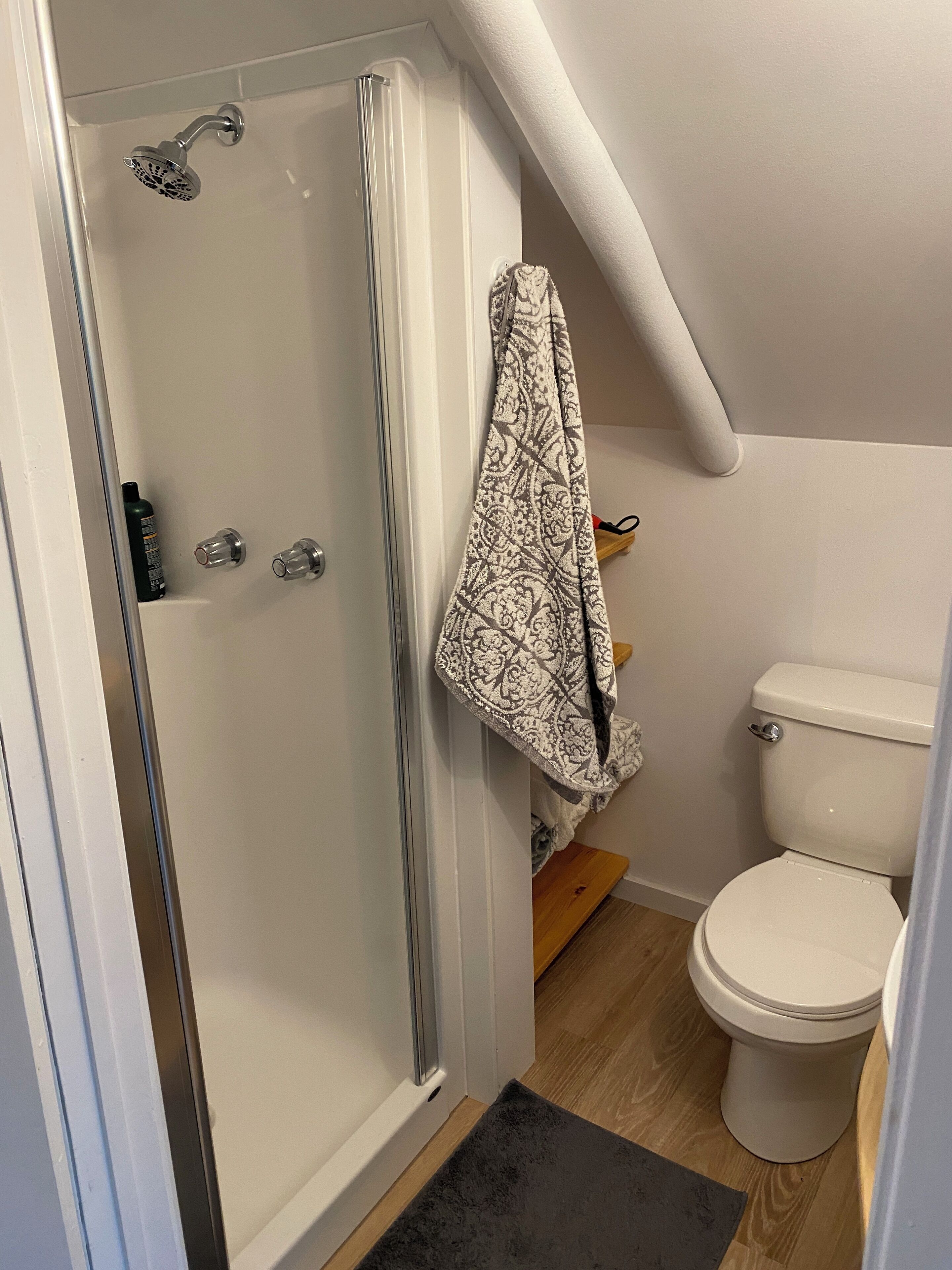 Un baño con cabina de ducha de vidrio, inodoro y toalla colgada en un perchero.