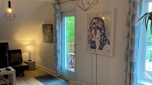A modern living room with a wooden dining table, a sofa, and a TV. There are two pendant lights, a door leading outside, and a window with curtains. - Apartment for rent in Bromont - 1 bedroom 1 bathroom (Bromont)