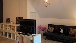 A modern living room with a flat-screen TV, a white entertainment unit, a black sofa with patterned cushions, and a geometric pendant light. - Apartment for rent in Bromont - 1 bedroom 1 bathroom (Bromont)