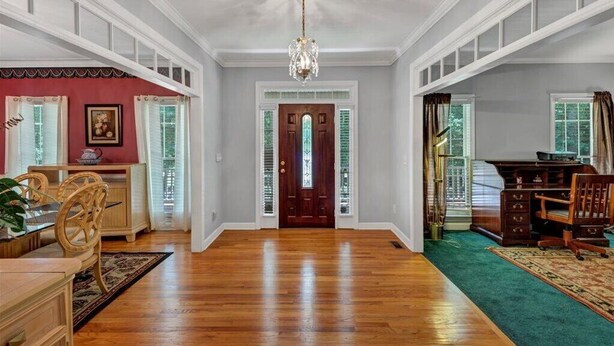A spacious room with hardwood flooring, a chandelier, a wooden desk, and a green carpet.