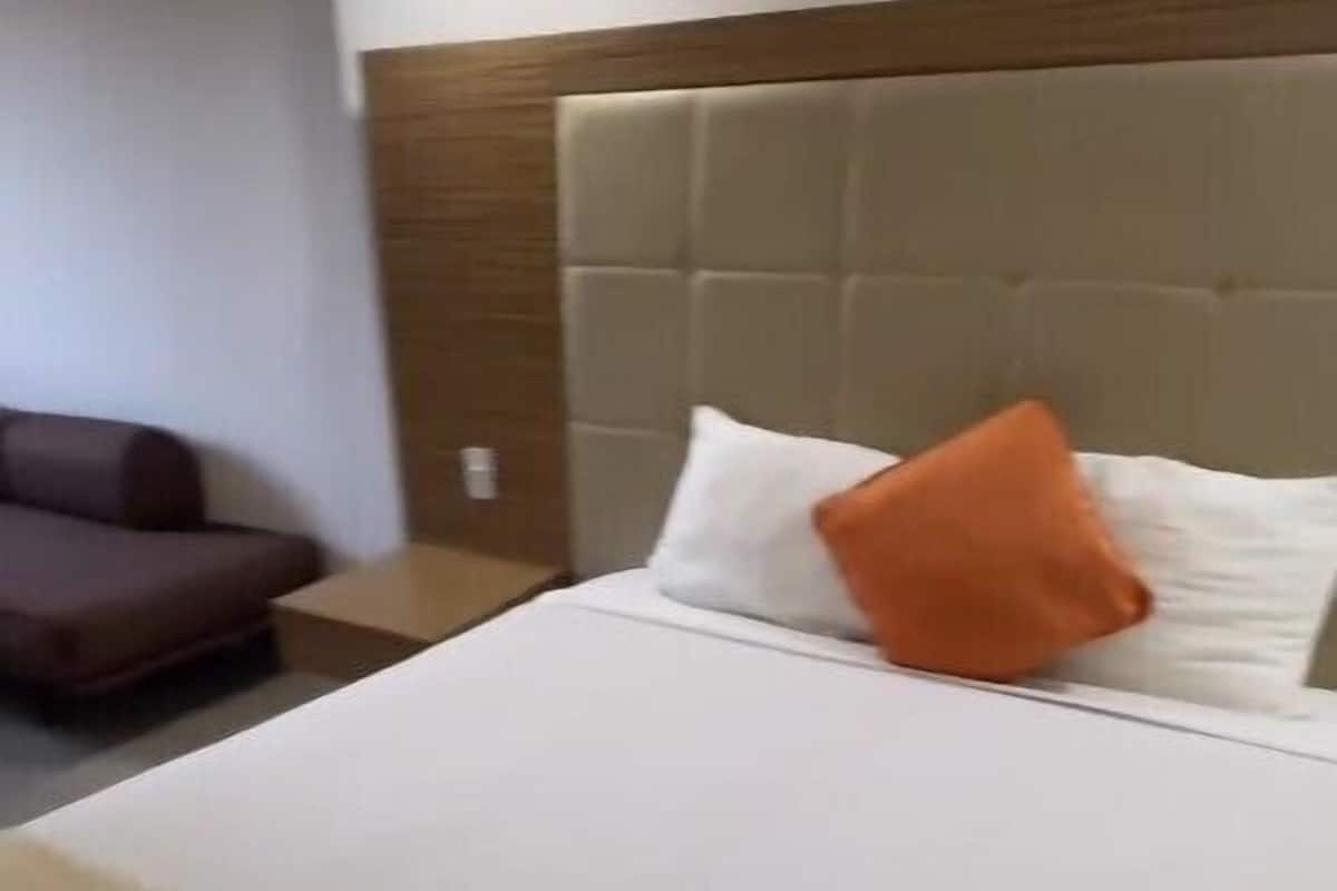 A hotel room with a large bed, a headboard, a brown sofa, and a small table.