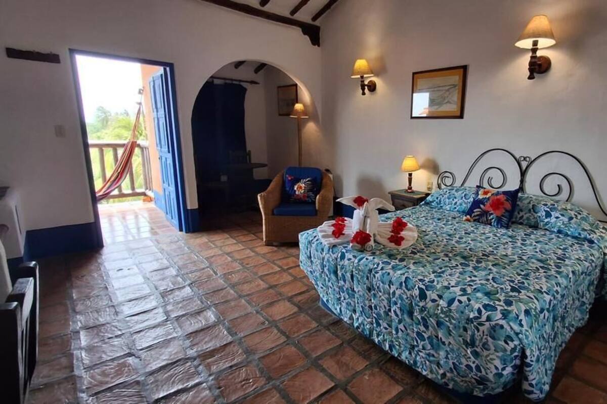 A bedroom with a bed, two bedside lamps, a chair, and a view of a balcony.