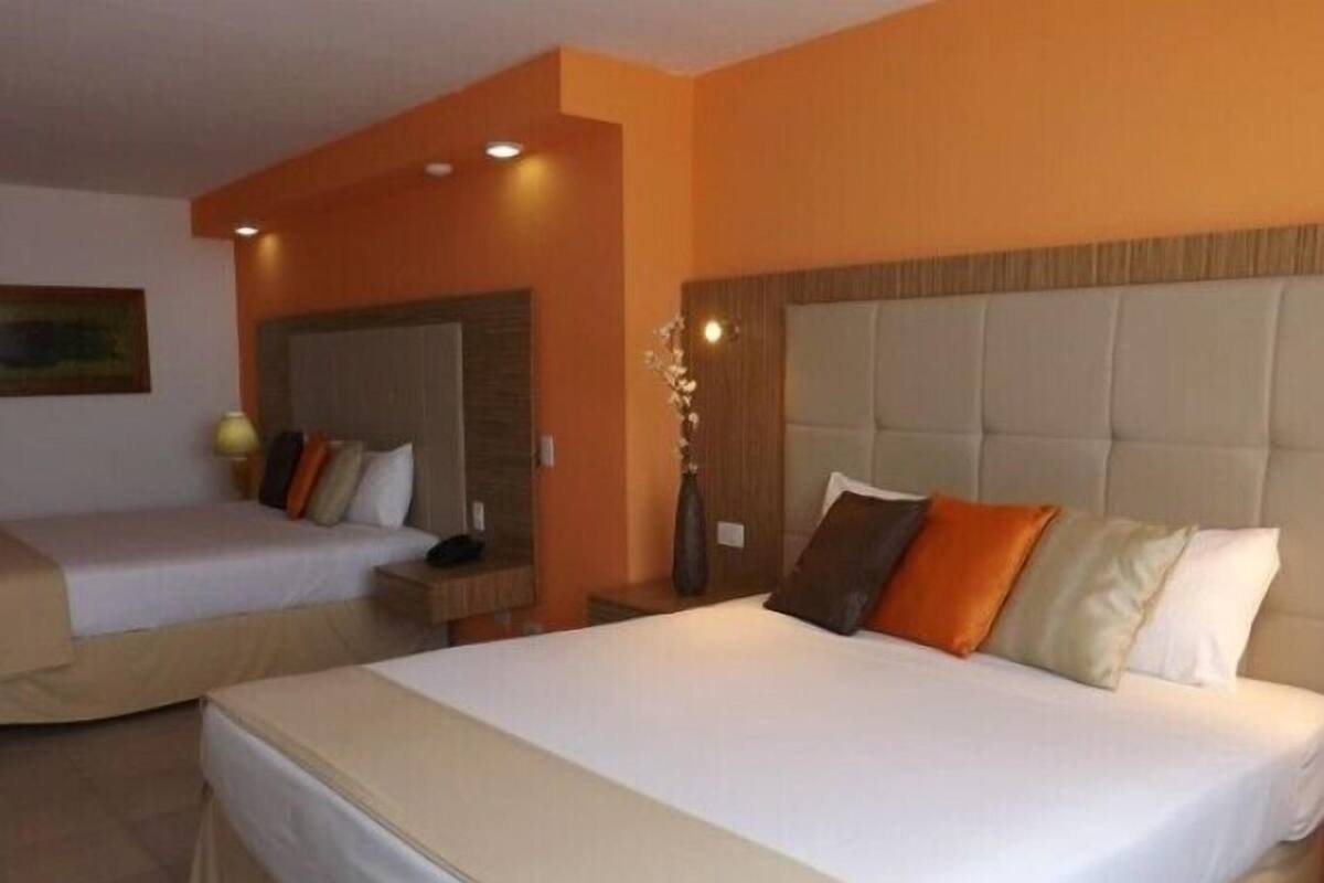 A hotel room with two beds, a wooden headboard, a nightstand, and a vase with flowers.