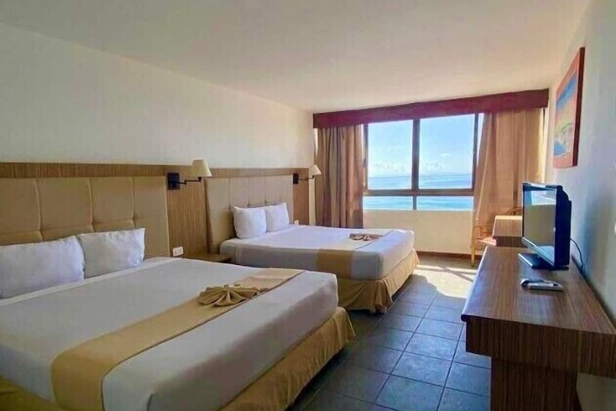 A hotel room with two beds, a desk, and a TV.