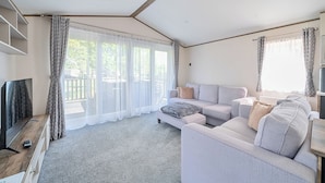 A modern living room with a sofa set, a flat-screen TV, and a large window with curtains.