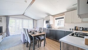 A modern kitchen with a dining area, featuring a wooden table, grey chairs, and a built-in microwave.