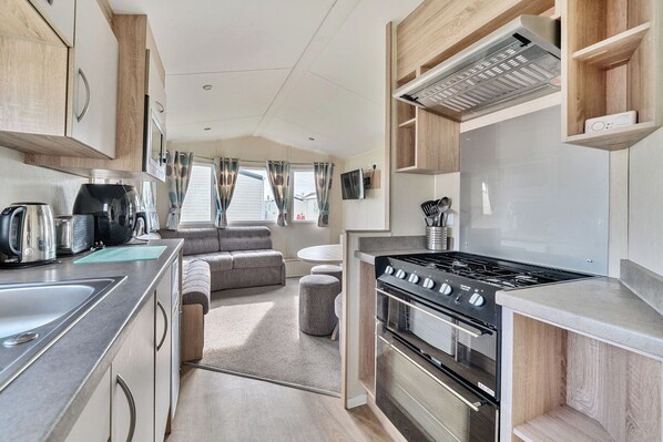 A compact RV kitchen with a stove, oven, and a dining area with a sofa. - The Lookout - Hayling Island (Hayling Island)