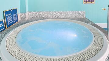 A hot tub with a tiled edge, surrounded by a pool area with a blue and white tiled floor.