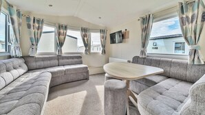 A caravan interior with a sofa set, a small table, and curtains. - The Lookout - Hayling Island (Hayling Island)