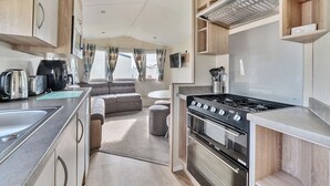 A compact RV kitchen with a stove, oven, and a dining area with a sofa. - The Lookout - Hayling Island (Hayling Island)