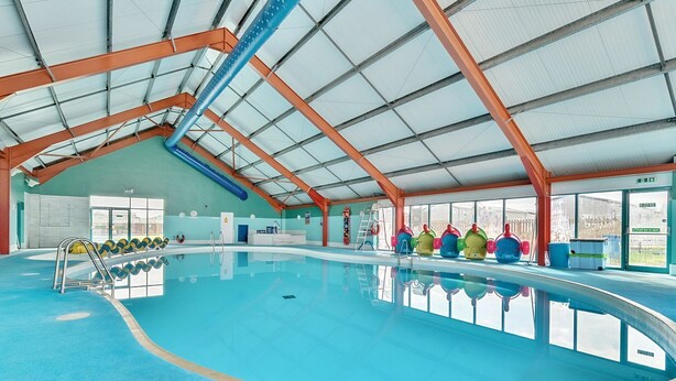 An indoor swimming pool with a high ceiling, clear windows, and colorful poolside chairs. - The Lookout - Hayling Island (Hayling Island)