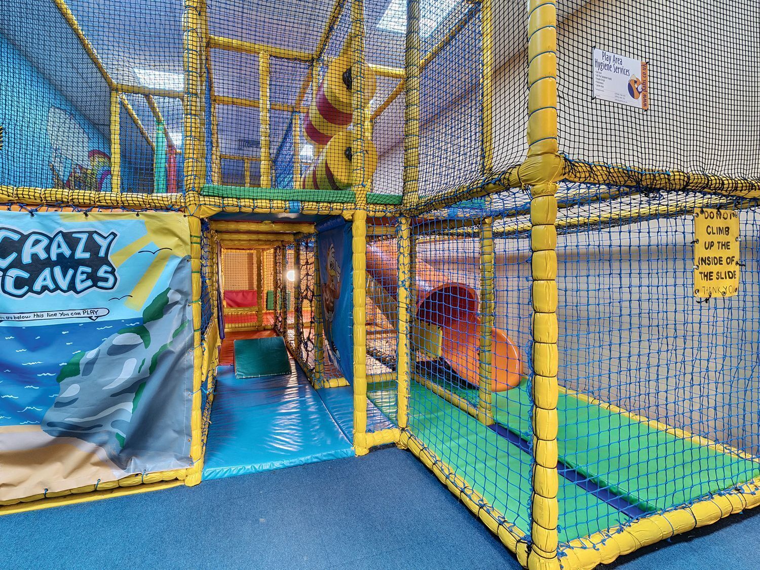 An indoor play area with a netted enclosure, a slide, and a 'Crazy Caves' themed entrance.