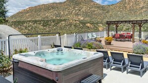A hot tub on a deck with a mountain view, outdoor seating, and a pergola.