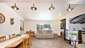 A dining area with a wooden table and chairs, a beige sofa, and a large window.
