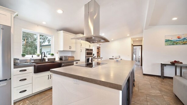 A modern kitchen with white cabinetry, a large island, stainless steel appliances, and a view of the outdoors.