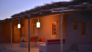 A cozy outdoor seating area with a thatched roof, a sofa, and a bench, illuminated by hanging lights. - HOSTAL VALLE DE LA LUNA  (Antofagasta)