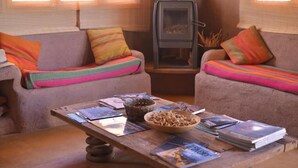 A cozy living room with two sofas, a wooden coffee table with books and a bowl, and a wood-burning stove. - HOSTAL VALLE DE LA LUNA  (Antofagasta)