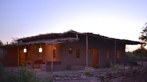 A rustic house with a thatched roof, a porch with seating, and a well-lit interior. - HOSTAL VALLE DE LA LUNA  (Antofagasta)