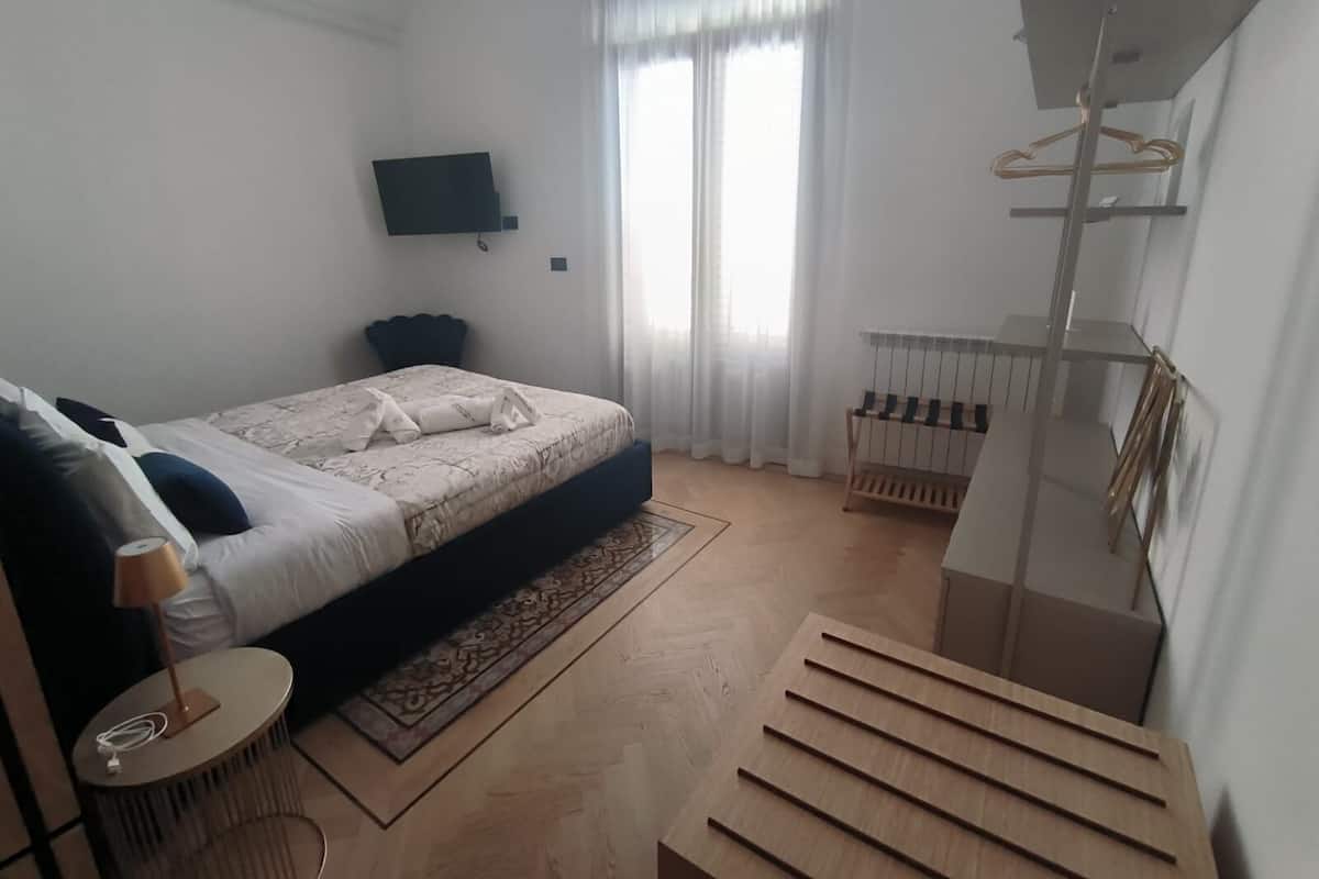 A modern bedroom with a bed, bedside table, lamp, and a view of the outside through a window.