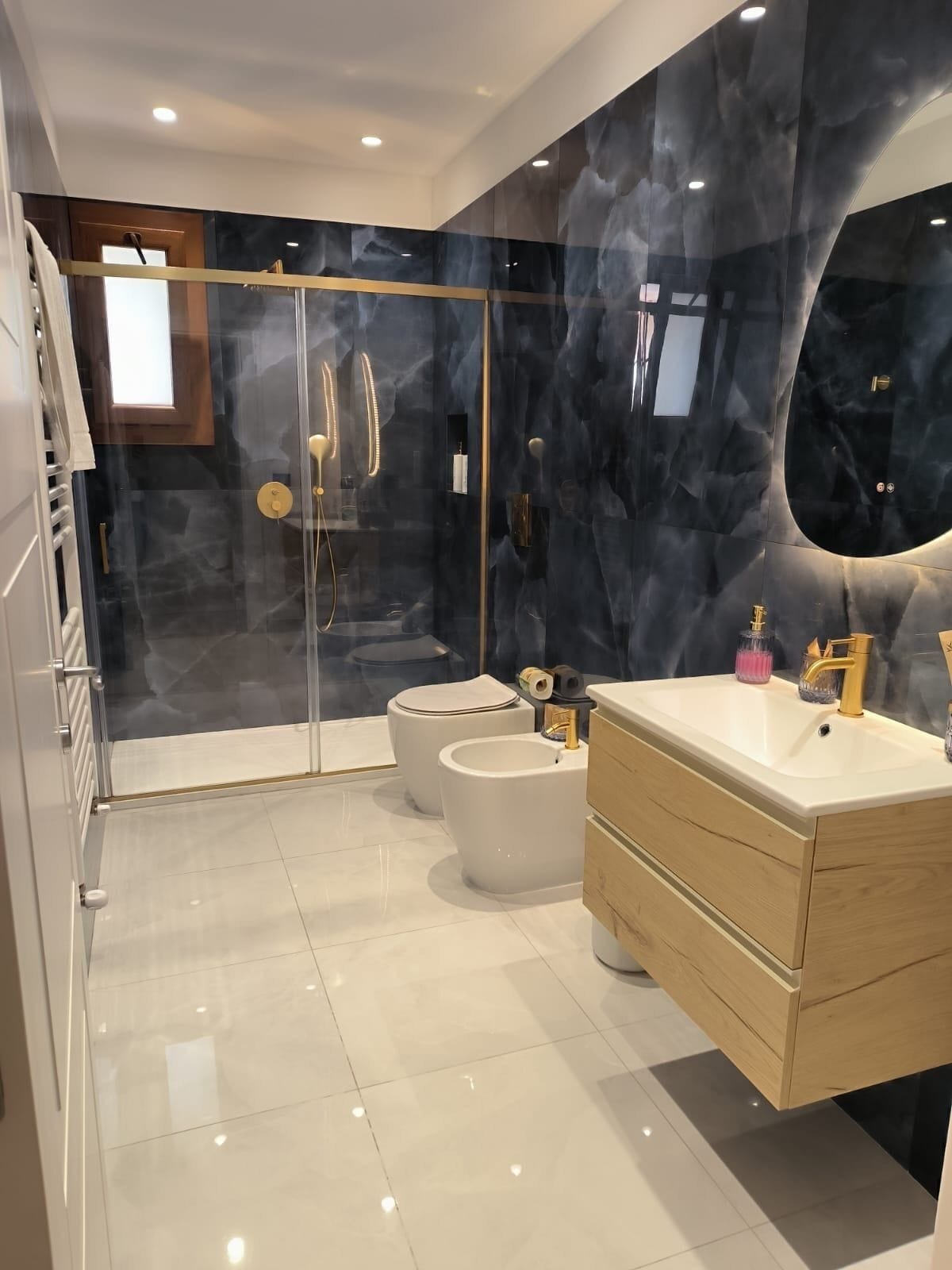 A modern bathroom with a glass-enclosed shower, two toilets, a bidet, and a vanity with a mirror.