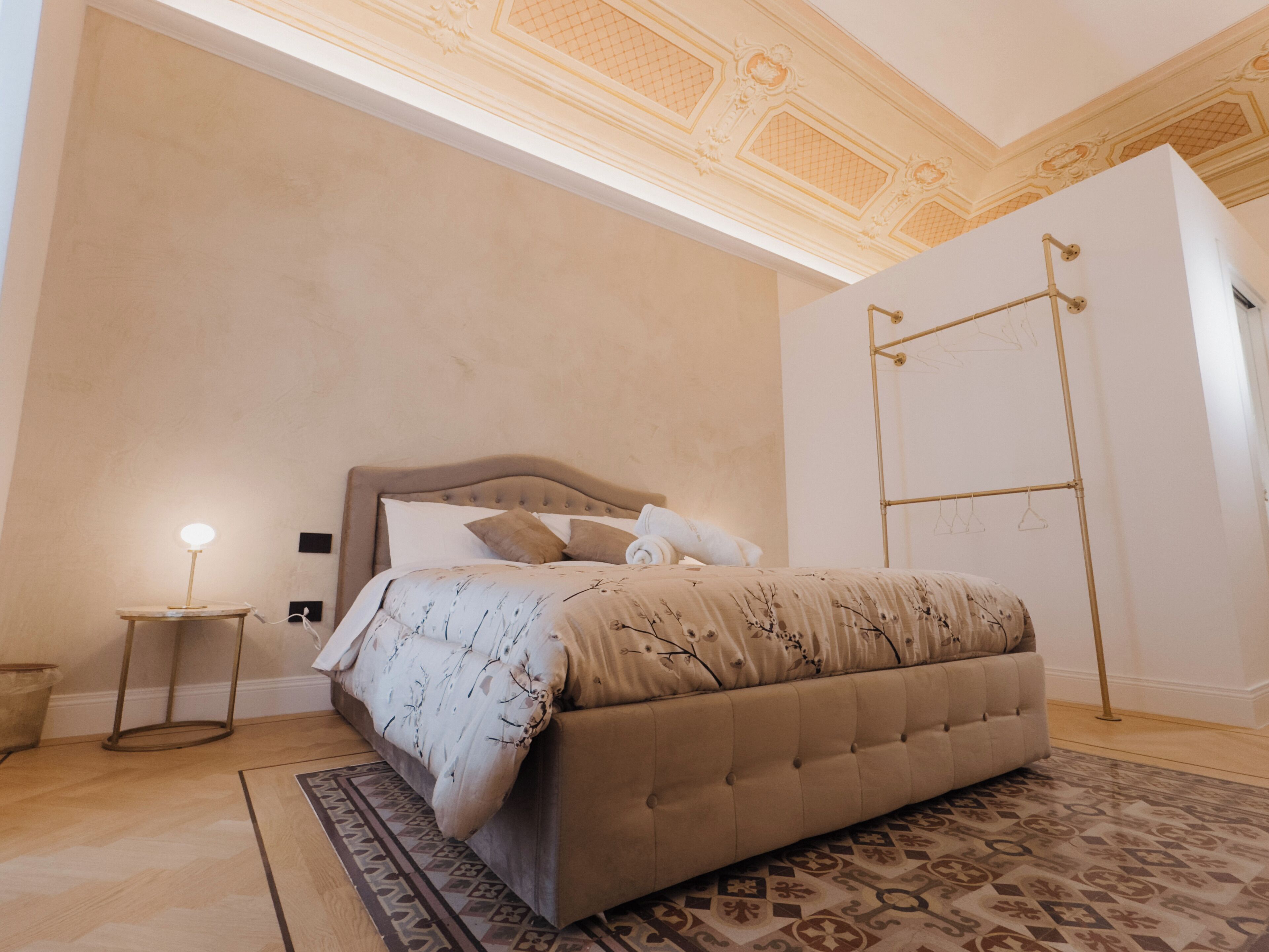 A bedroom with a large bed, a bedside table with a lamp, a patterned rug, and a decorative ceiling.