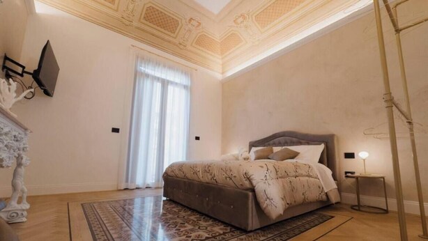A bedroom with a large bed, a decorative ceiling, and a patterned rug. - Butera505luxurysuites (Bagheria)
