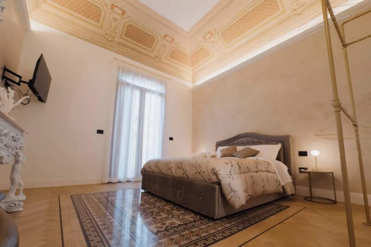 A bedroom with a large bed, a decorative ceiling, and a patterned rug.