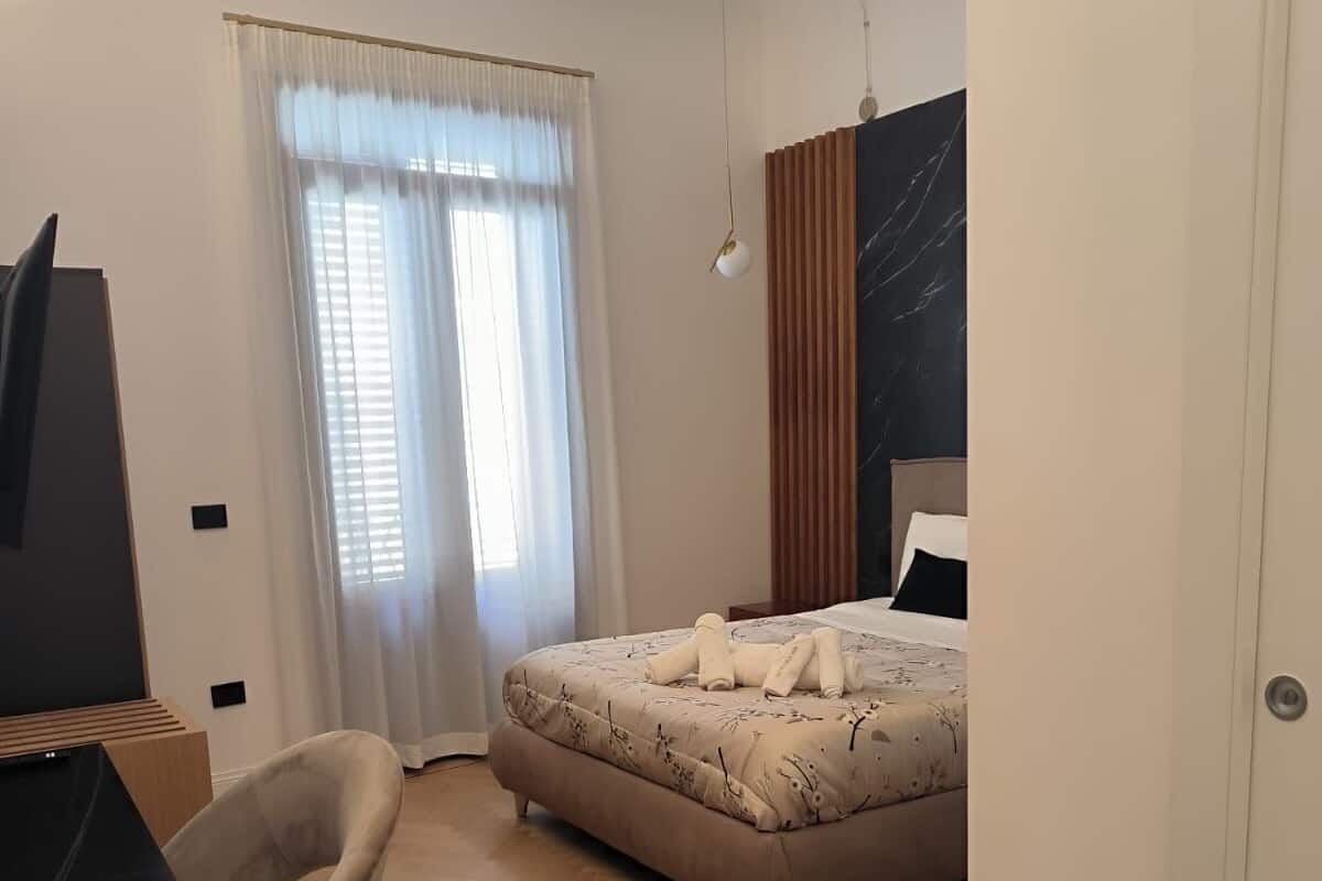 A hotel room with a bed, a desk with a computer, a chair, and a wardrobe.