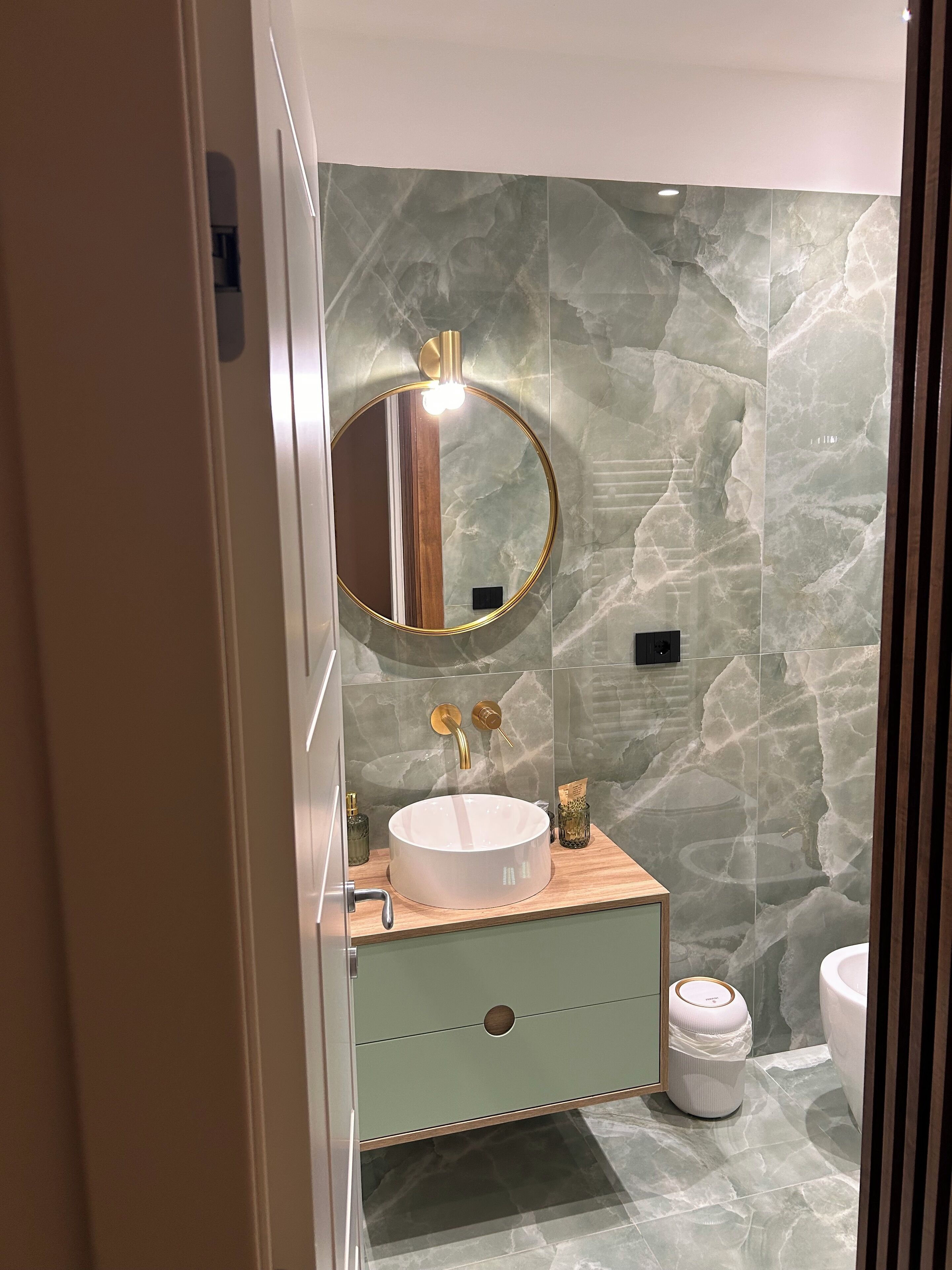 Une salle de bain moderne avec un miroir rond, un lavabo blanc et des toilettes.