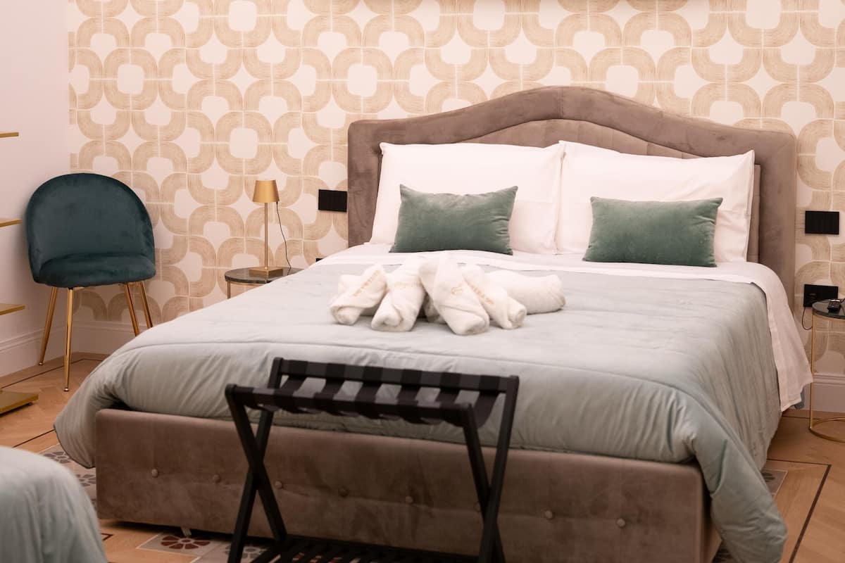 A bedroom with a bed, pillows, a bench, a chair, and a patterned rug.